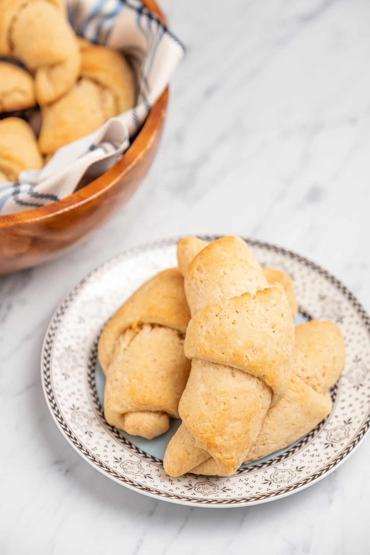 Three crescent rolls on a plate next to a bowl of more rolls.
