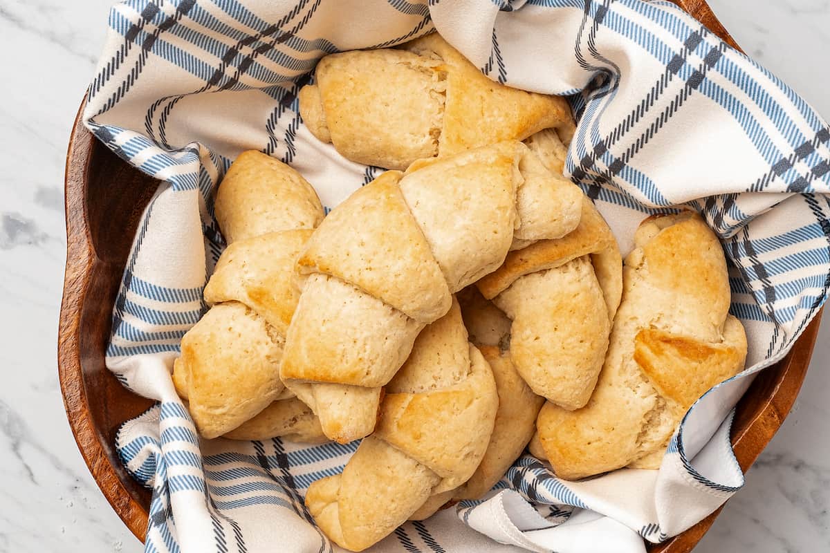Top view of assorted gluten free crescent rolls nestled in a bowl lined with a dishcloth.