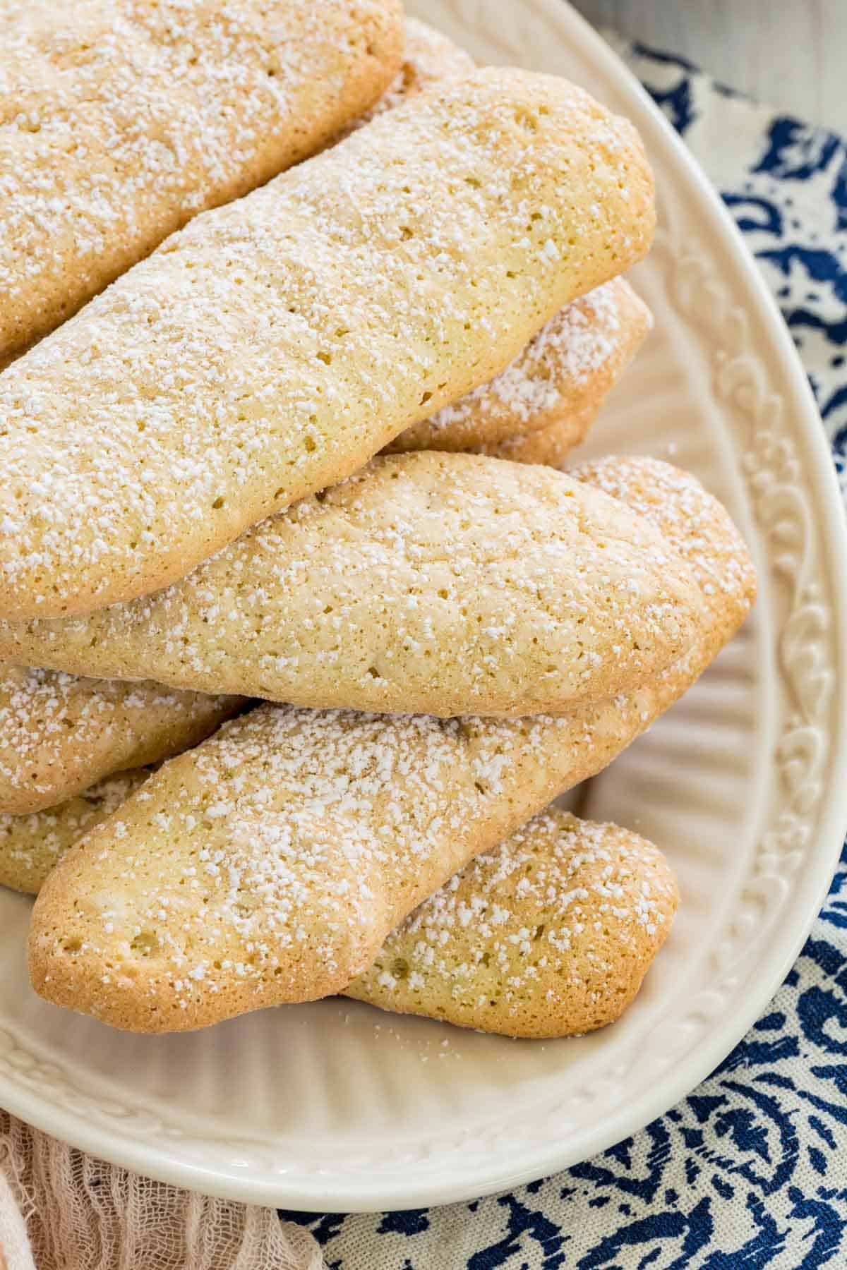 Top view of gluten free ladyfingers stacked on a white plate.