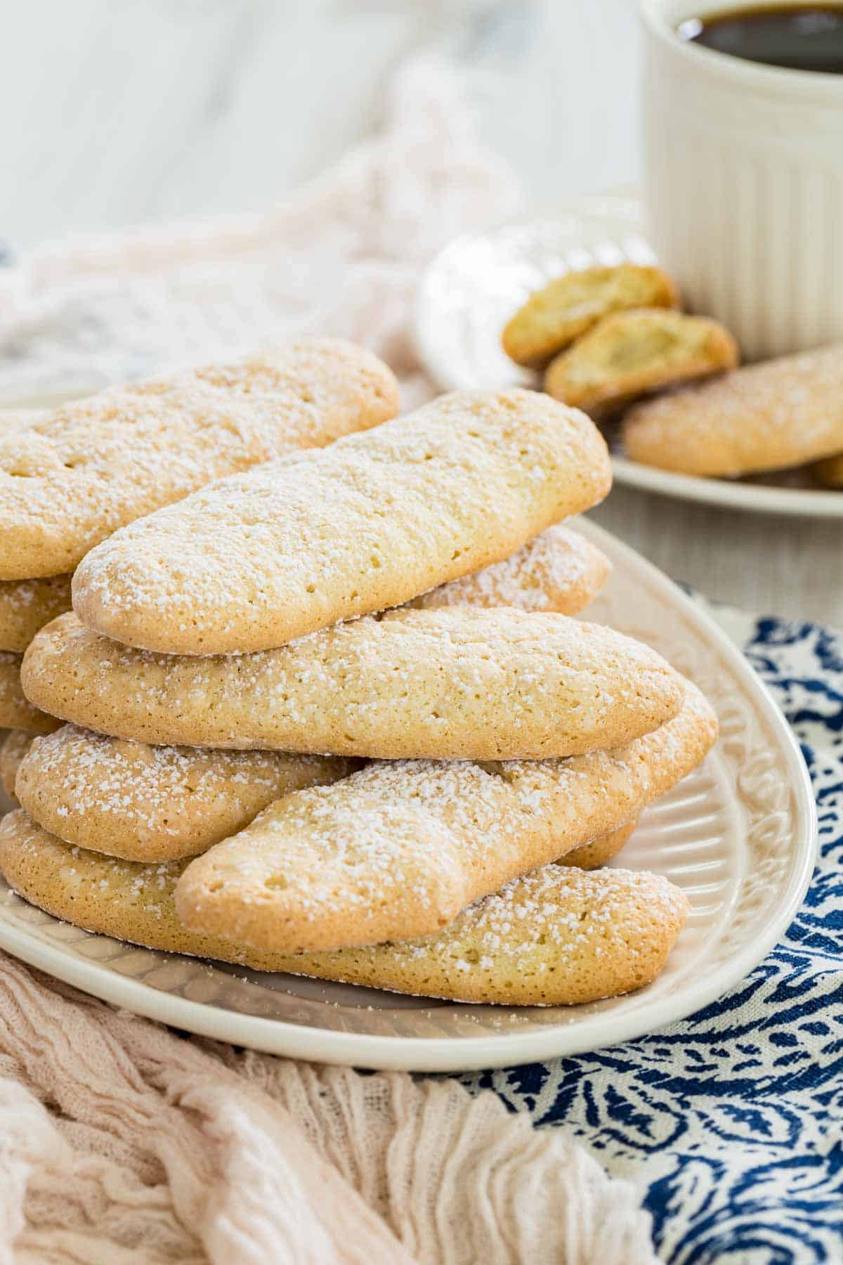 Gluten free ladyfingers stacked on a white plate, with a cup of coffee in the background.