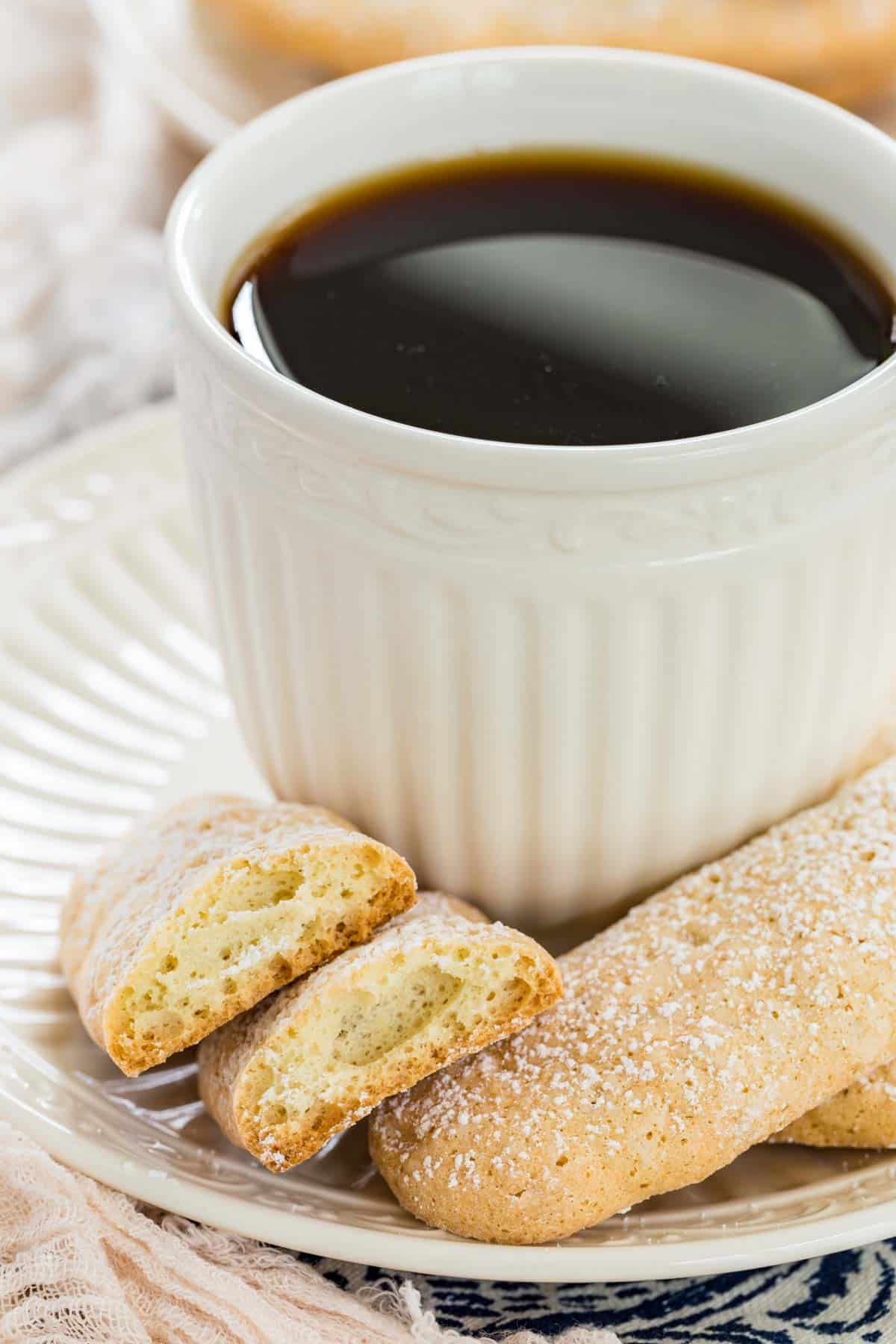 Gluten free ladyfingers on a saucer next to a cup of coffee.