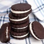 Four homemade gluten free oreos stacked on a plaid napkin with two cookies leaning against the stack with a bite in one of them.