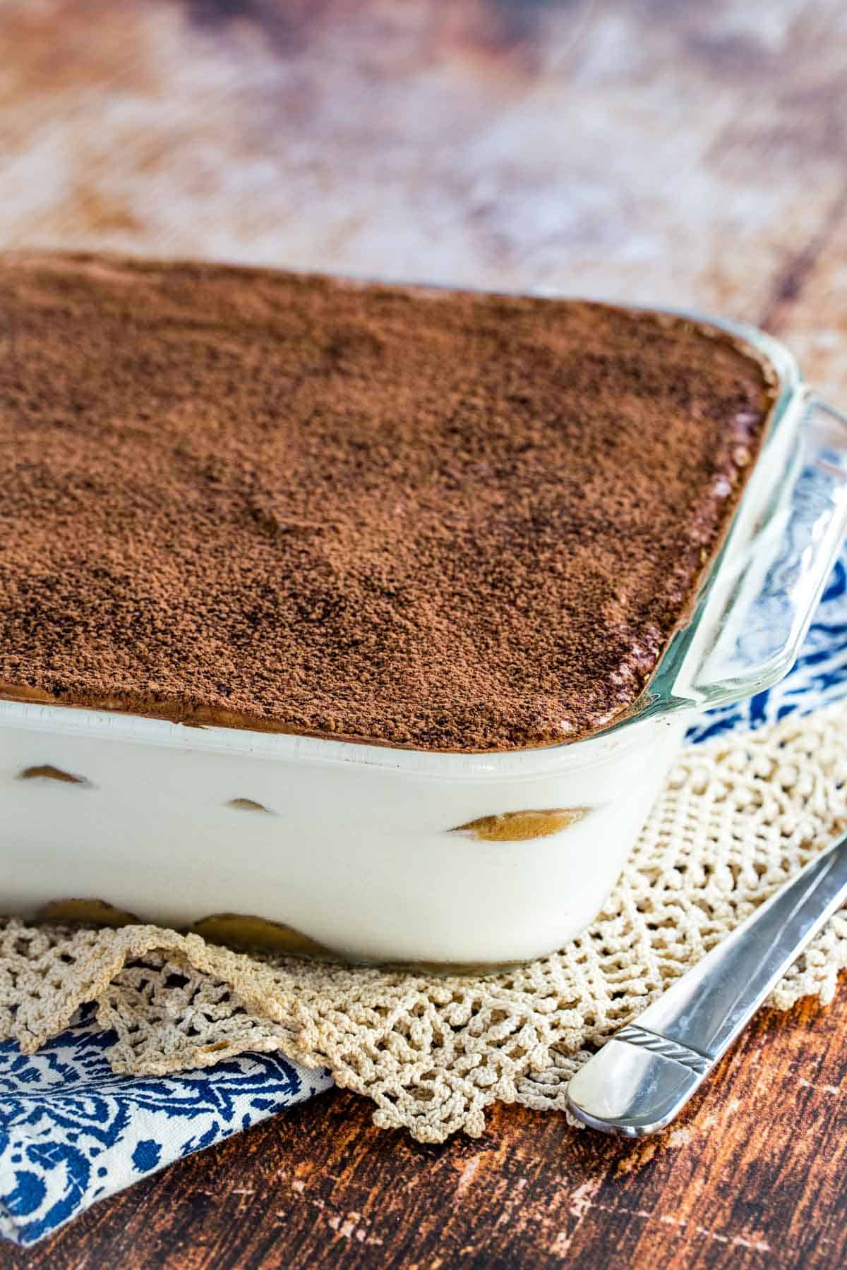 Gluten-free tiramisu dusted with cocoa powder inside a glass baking dish.