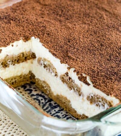 Gluten-free tiramisu dusted with cocoa powder inside a glass baking dish, with two servings missing.