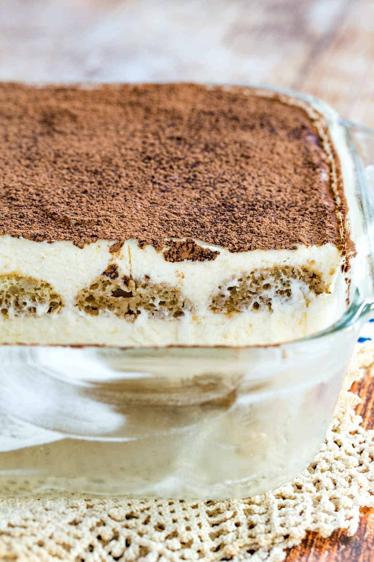Front view of gluten-free tiramisu dusted with cocoa powder inside a glass baking dish, with two servings missing.