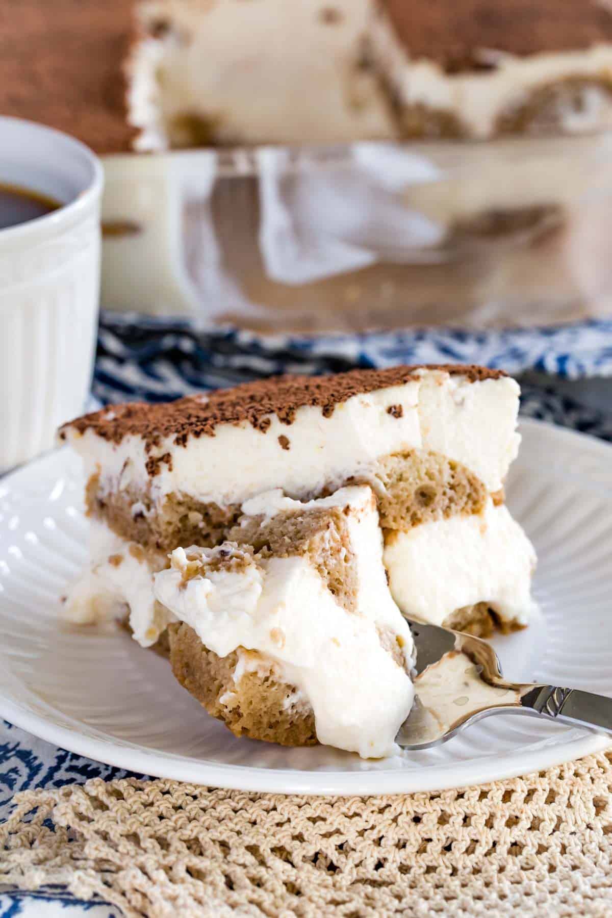 A fork inserted into a slice of gluten-free tiramisu on a white plate.