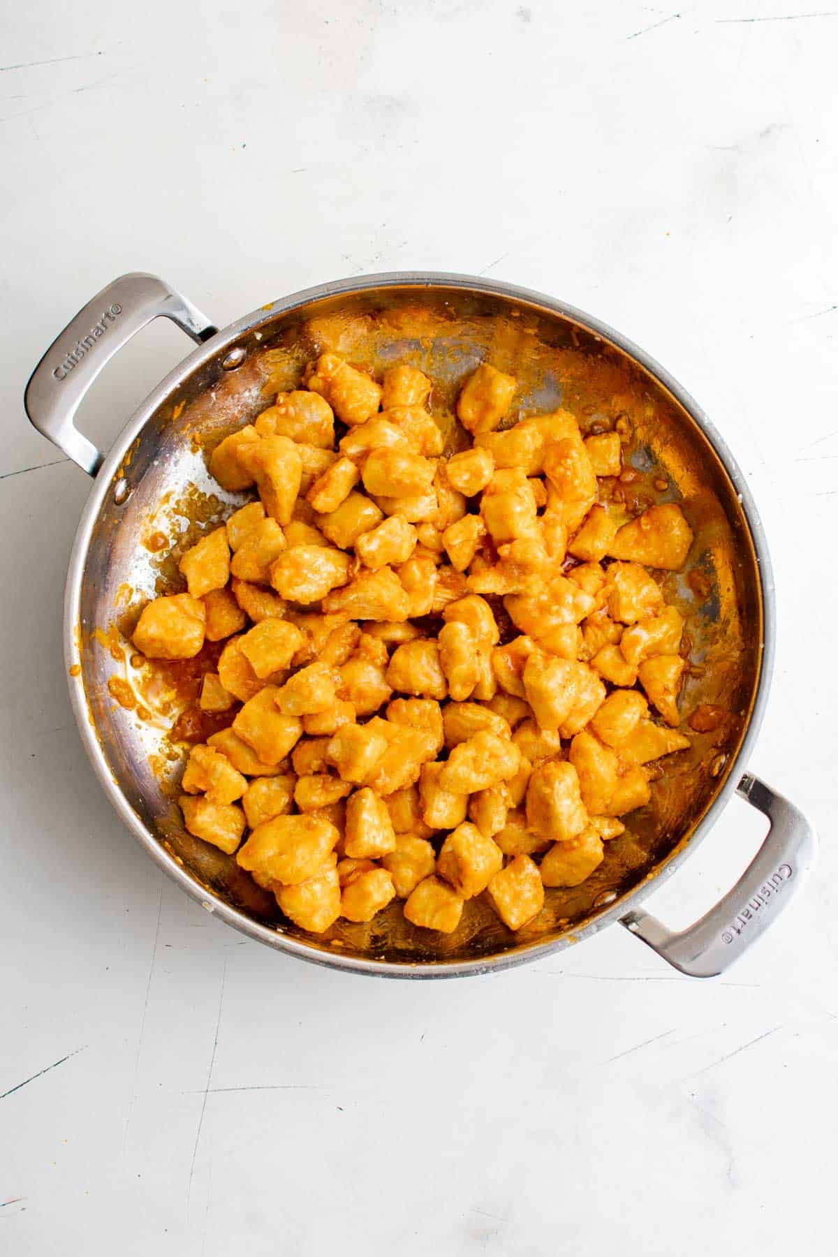 Top view of chicken bites coated in buffalo sauce in a metal skillet.
