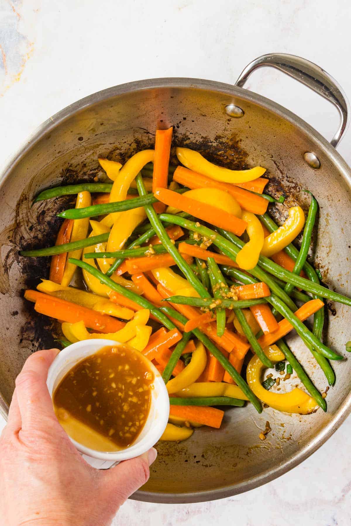 Pouring stir fry sauce over vegetables in a wok.