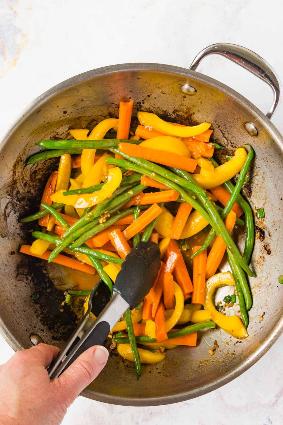 Tossing the veggies in a wok using tongs.