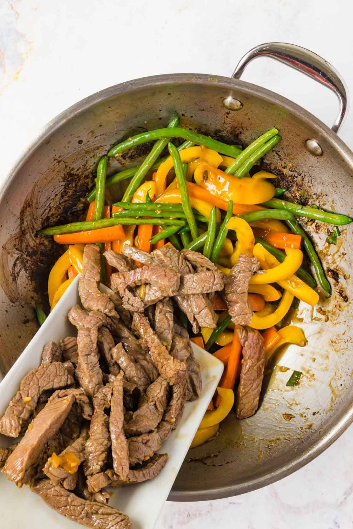 Adding browned sliced of beef back to the wok with the vegetables.