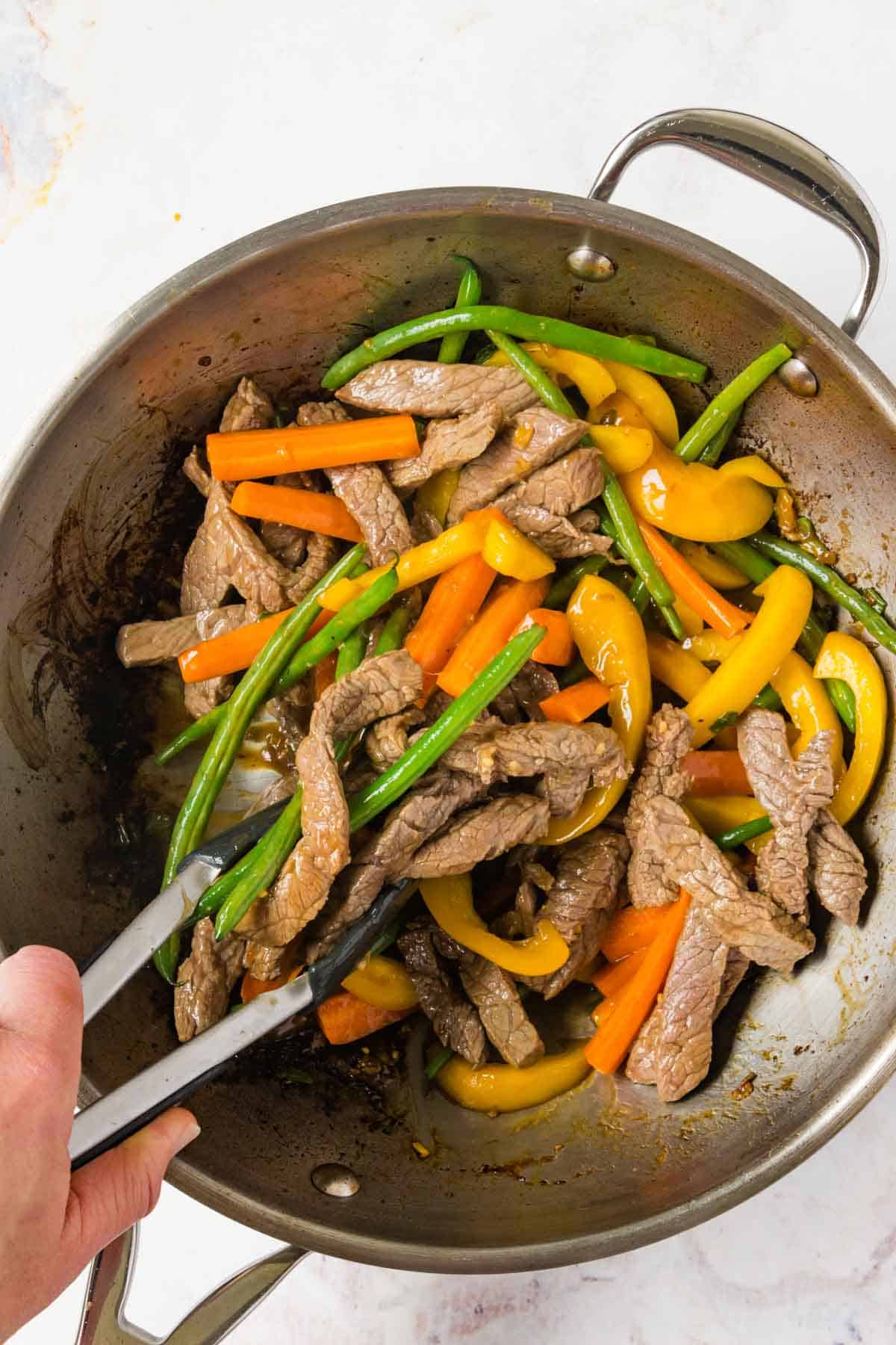 Tossing the beef and vegetable stir fry together in the a wok with tongs.