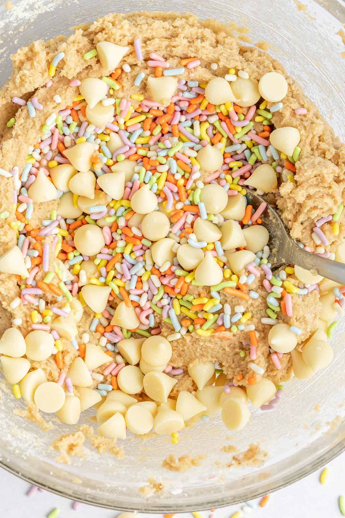Top view of gluten free birthday cake cookie dough in a glass mixing bowl with a spoon.