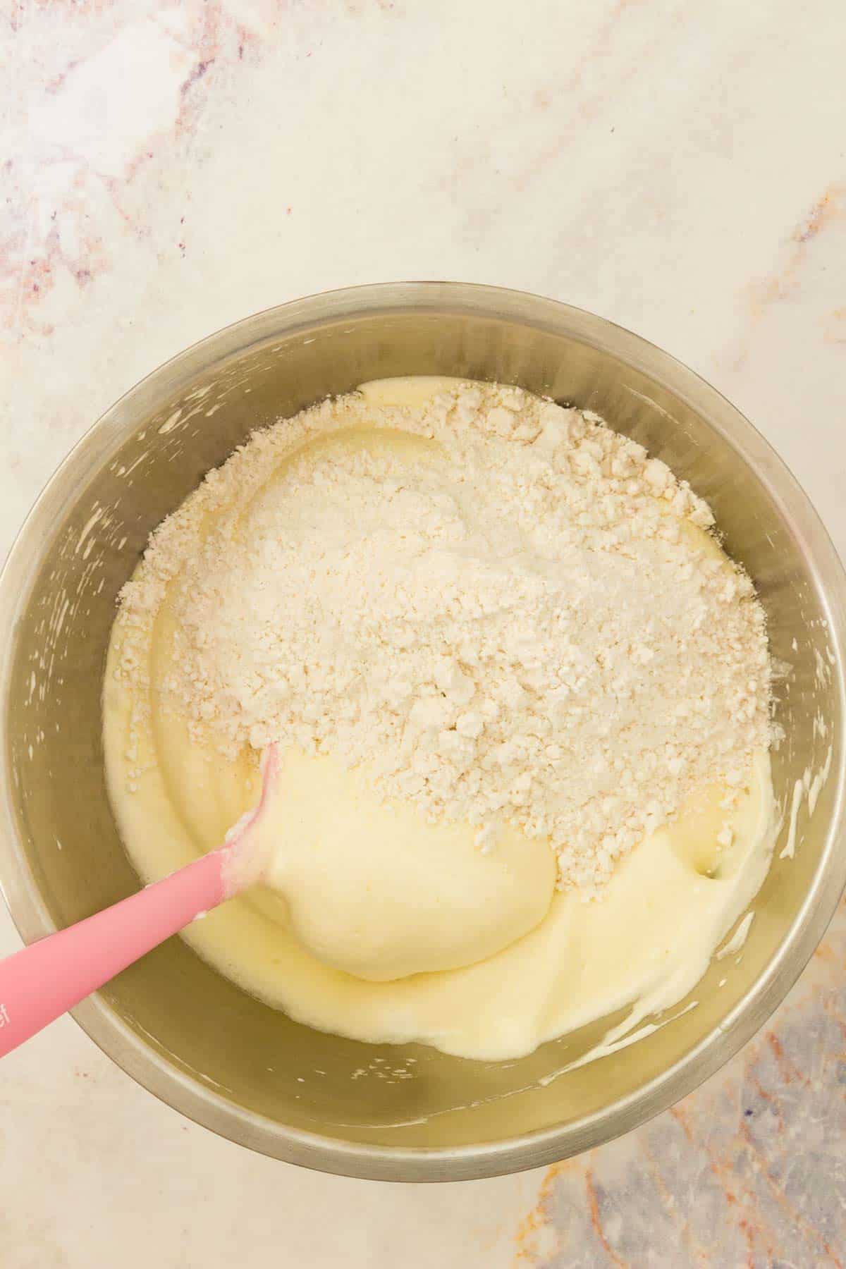Dry ingredients added to a bowl of whipped egg mixture for gluten free ladyfinger batter.