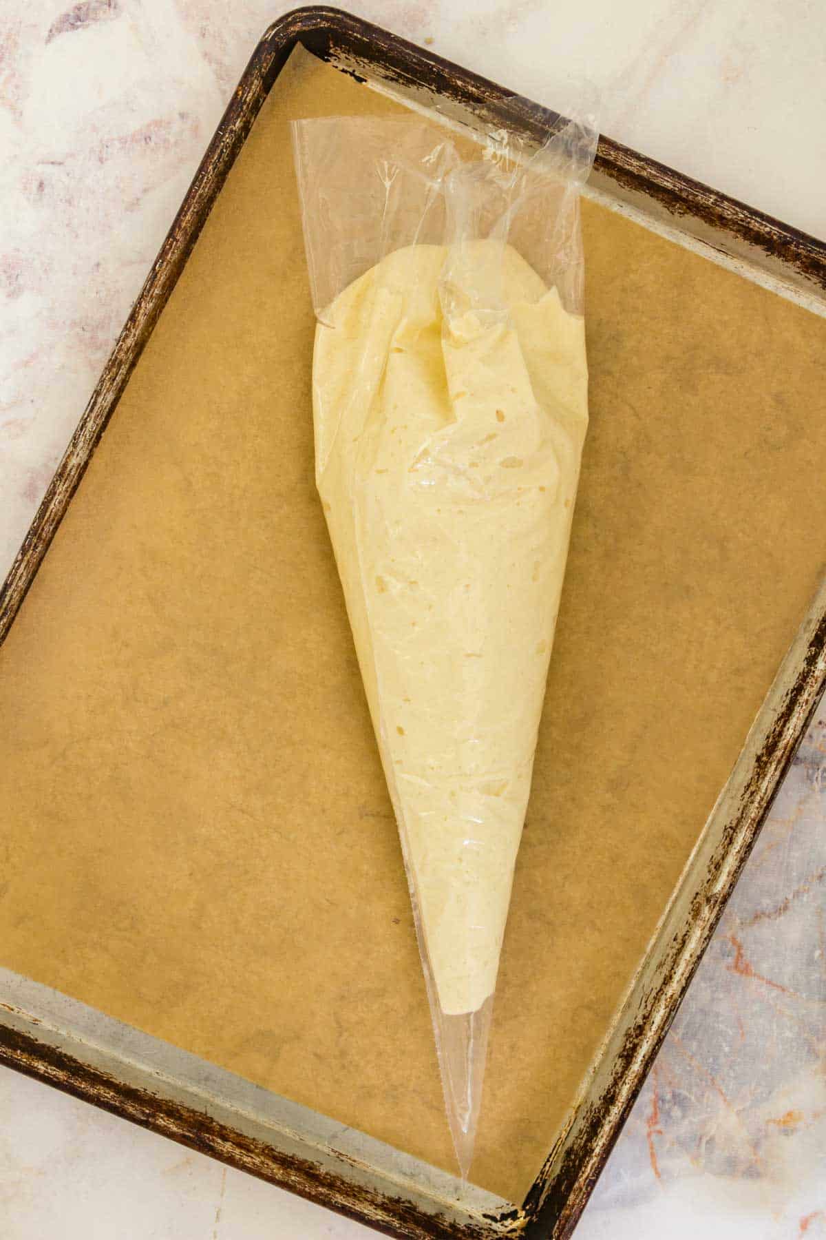 A piping bag filled with the batter for gluten free ladyfingers, resting on a parchment lined baking sheet.