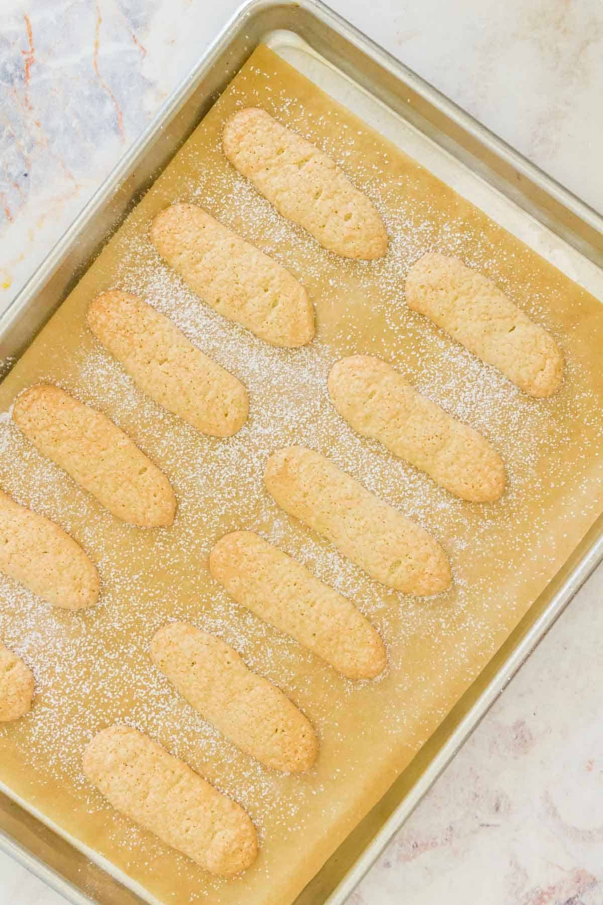 Baked gluten free ladyfingers on a baking sheet lined with parchment paper.