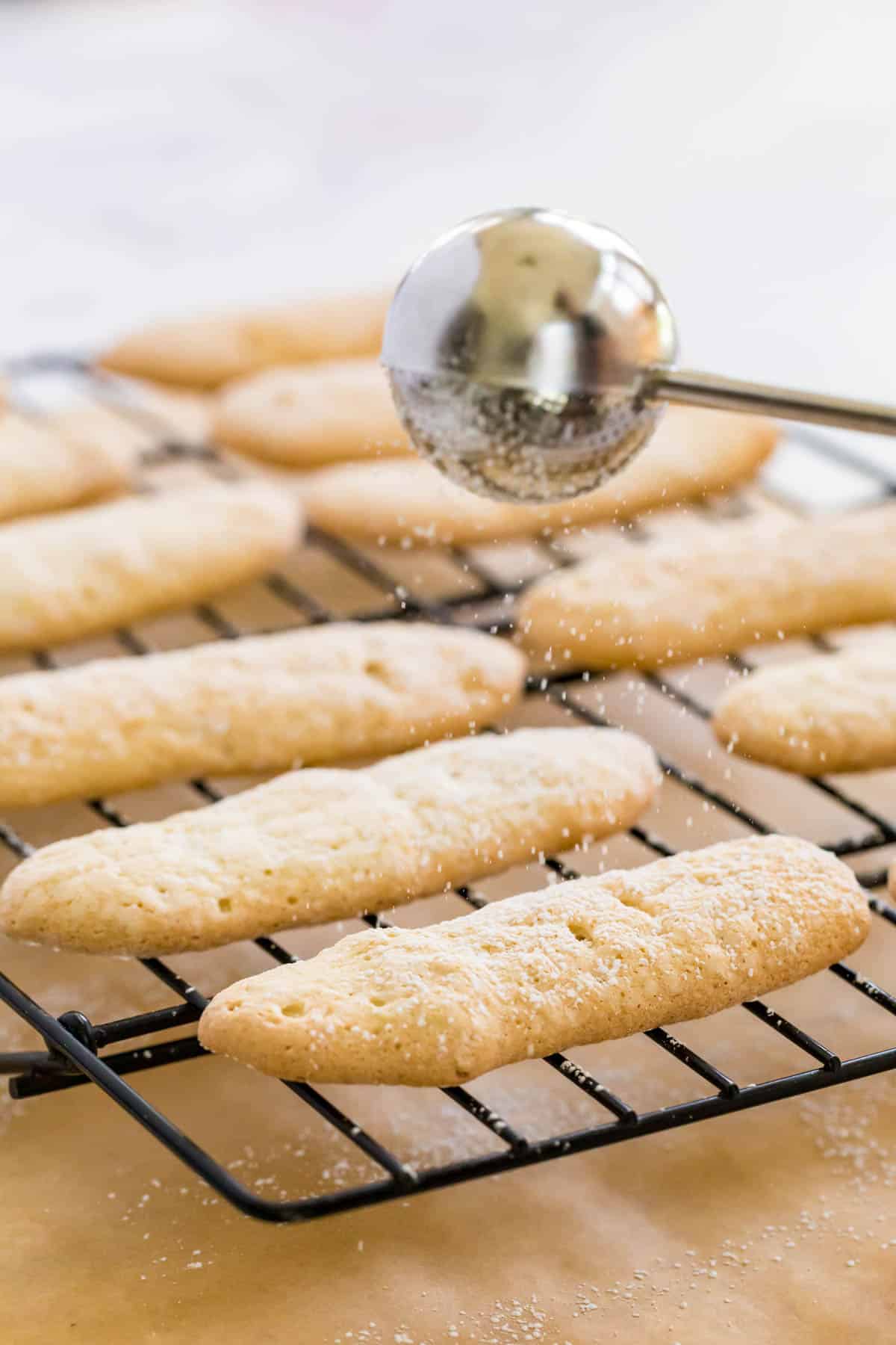 Gluten free ladyfingers are dusted with powdered sugar while cooling on a wire rack.