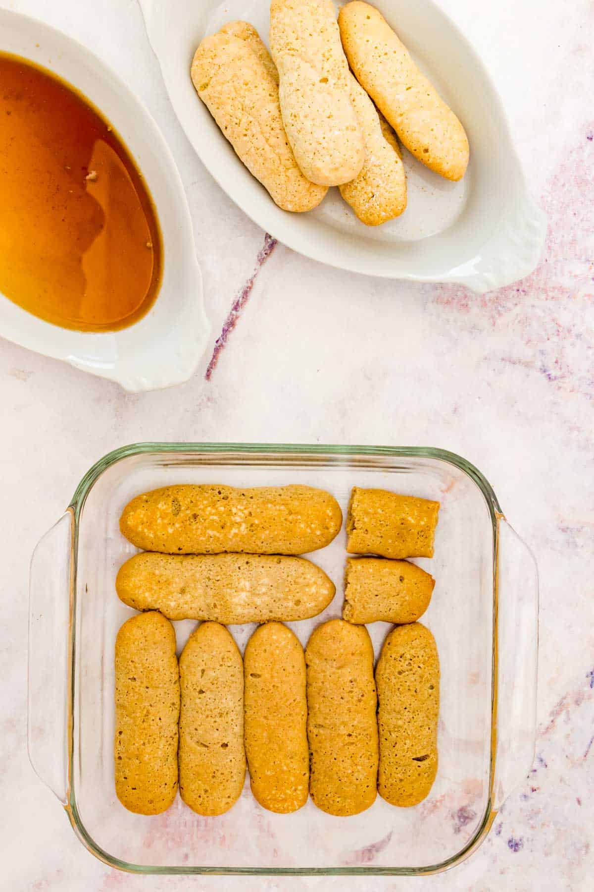 Ladyfingers dipped in espresso arranged in a single layer in the bottom of a glass baking dish.
