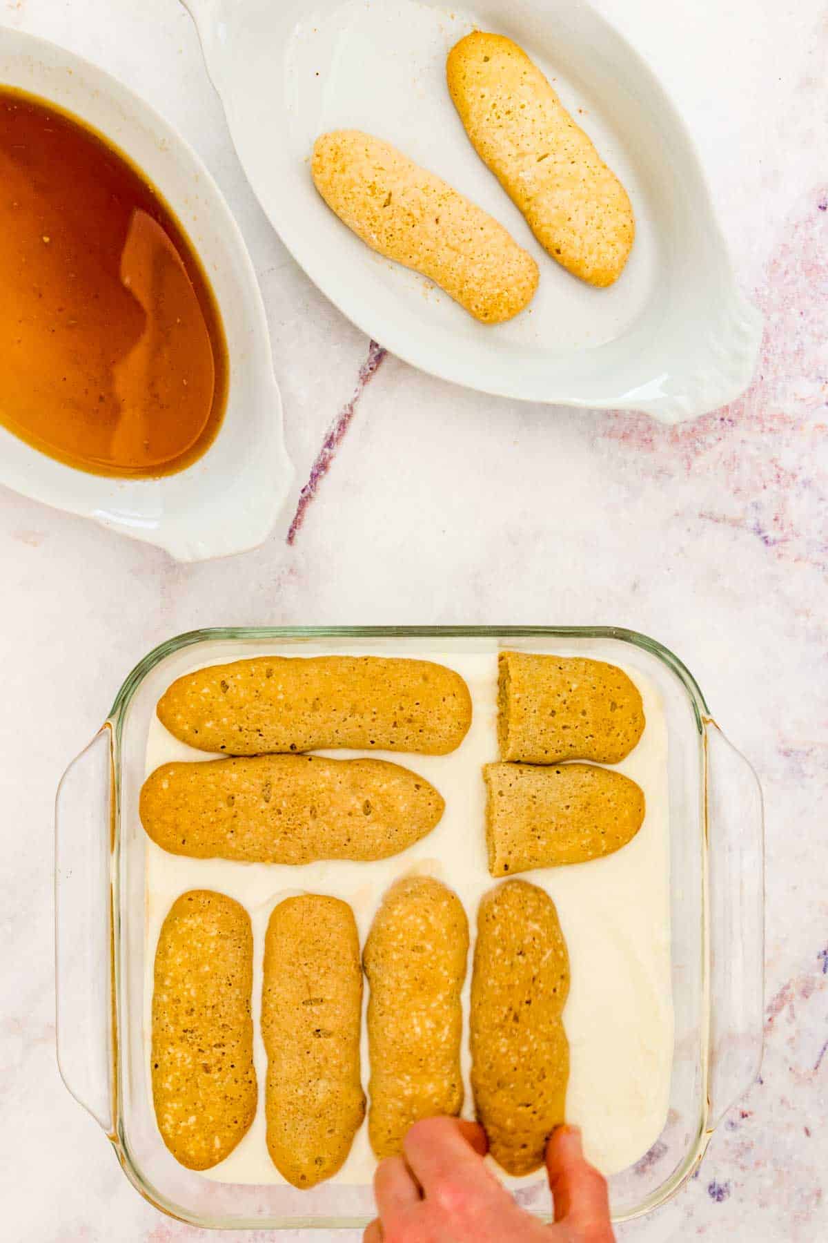 A layer of ladyfingers is placed over a layer of mascarpone inside a glass baking dish.