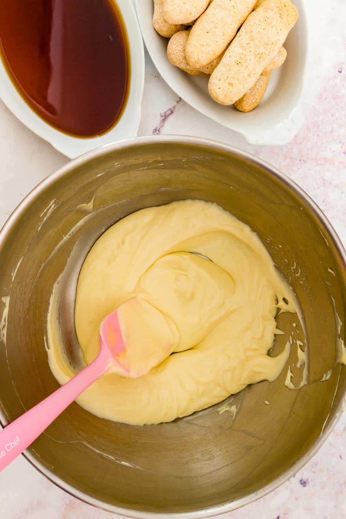 Egg yolks are stirred into the mascarpone mixture in a metal mixing bowl.