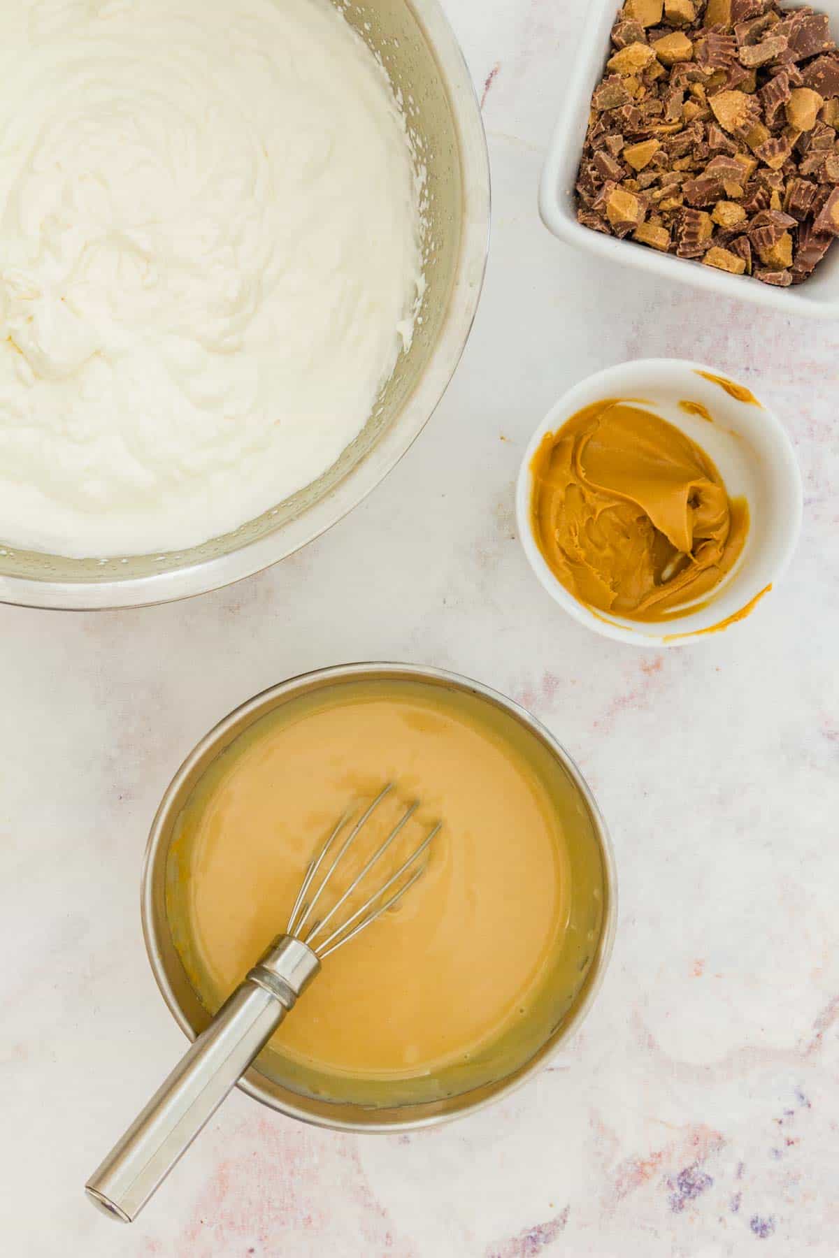 Sweetened condensed milk whisked together with peanut butter in a small bowl, next to a large metal bowl of whipped cream.