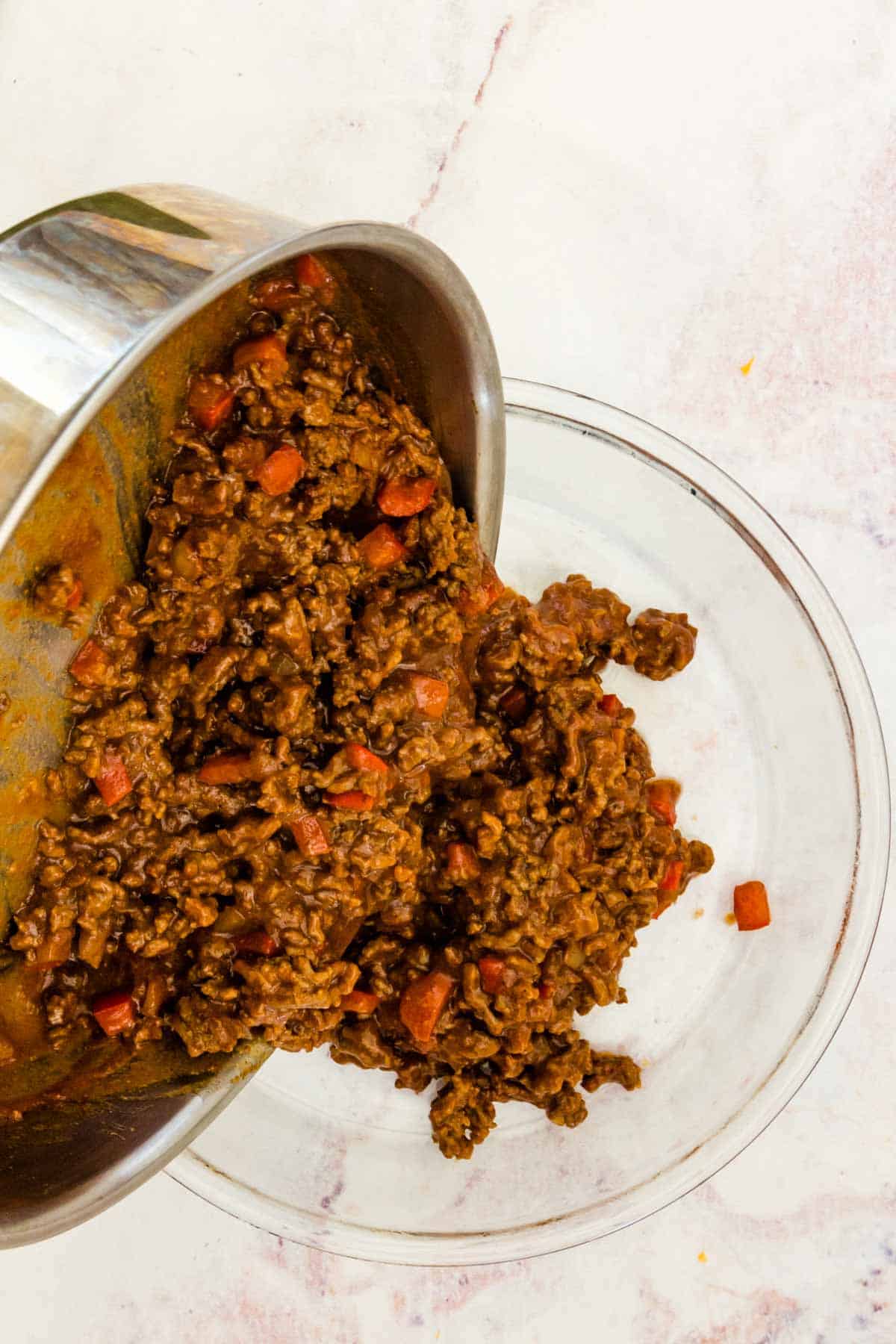 Sloppy joe mixture is poured from a skillet into a glass baking dish.
