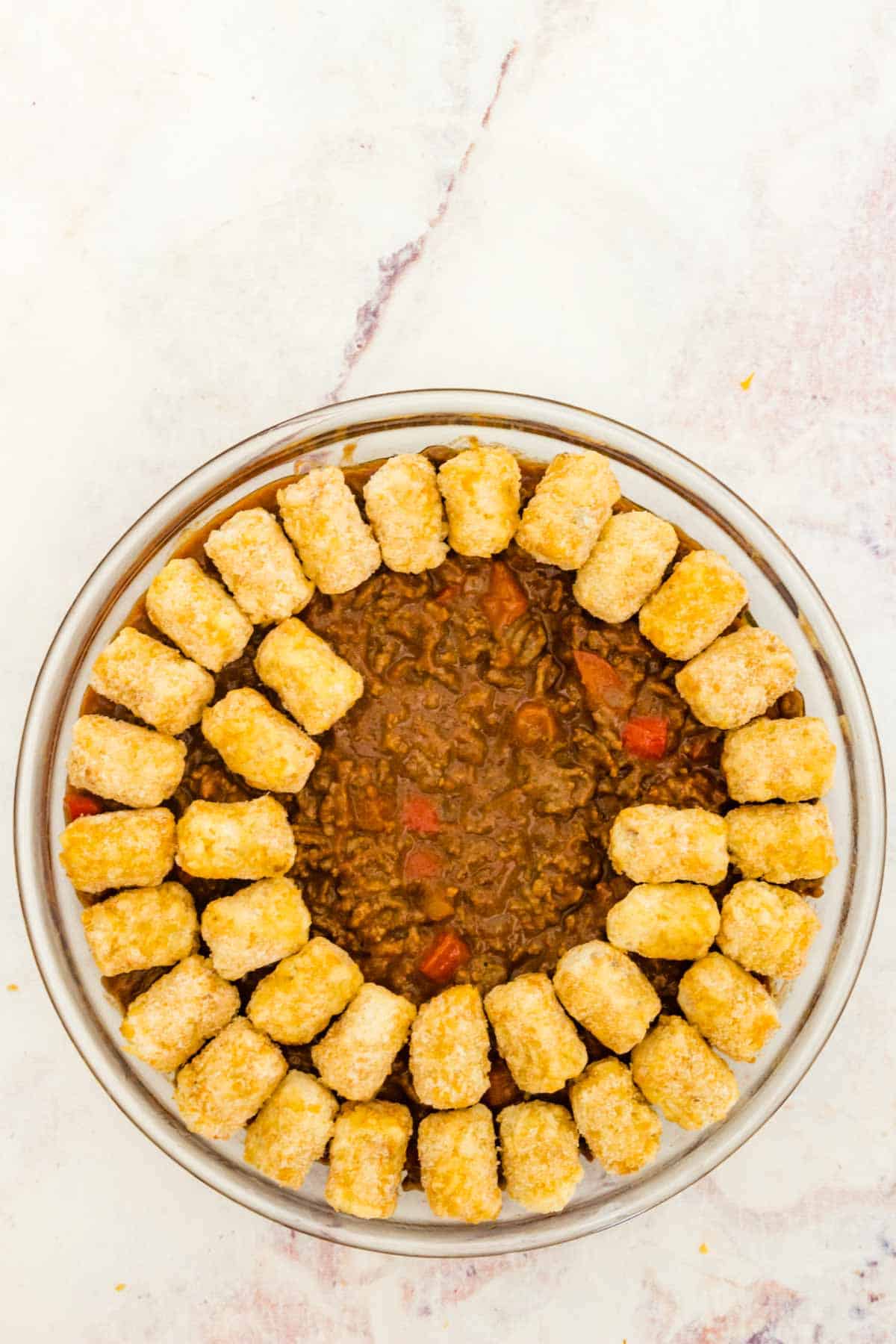 Tater tots are arranged in a single layer over top of the sloppy joe mixture in a glass baking dish.