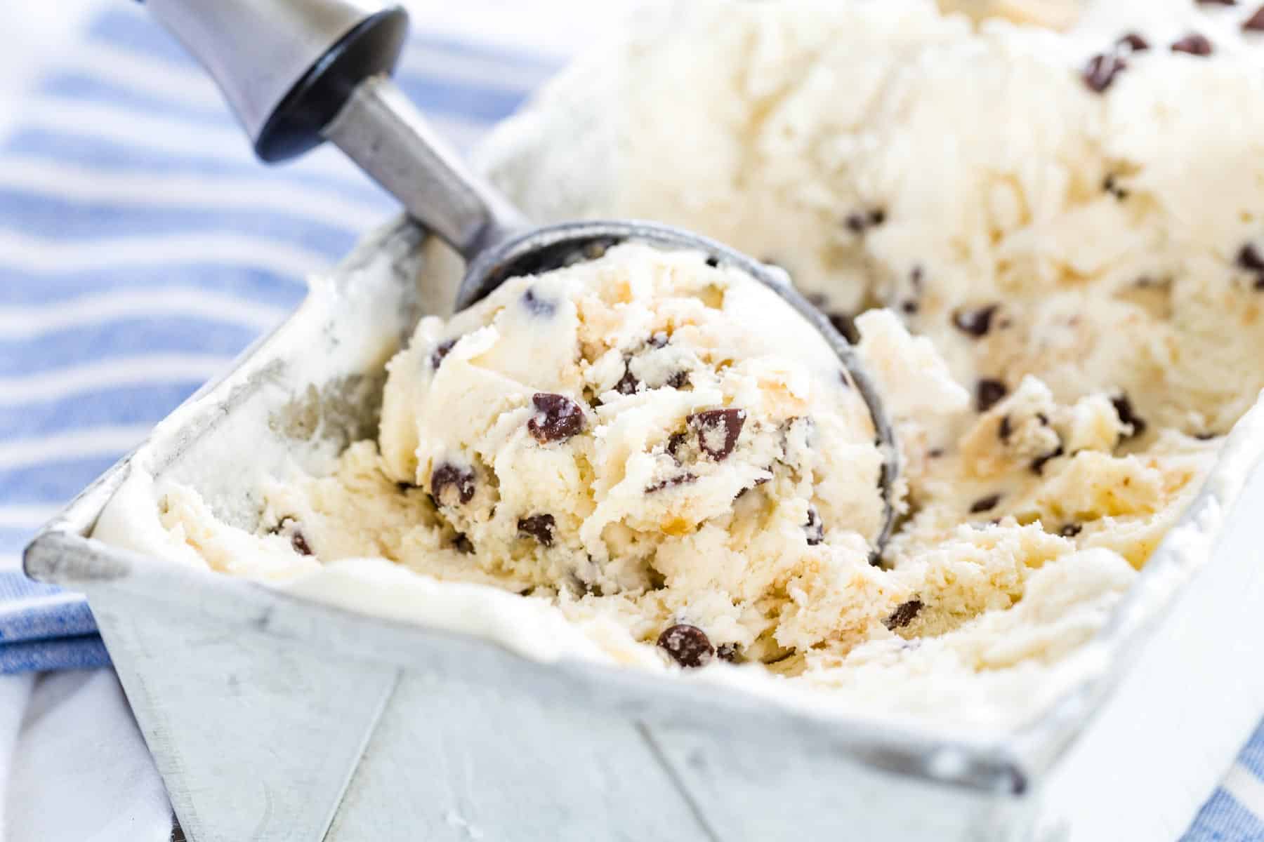 An ice cream scoop scooping up some cookie dough ice cream from a metal pan.