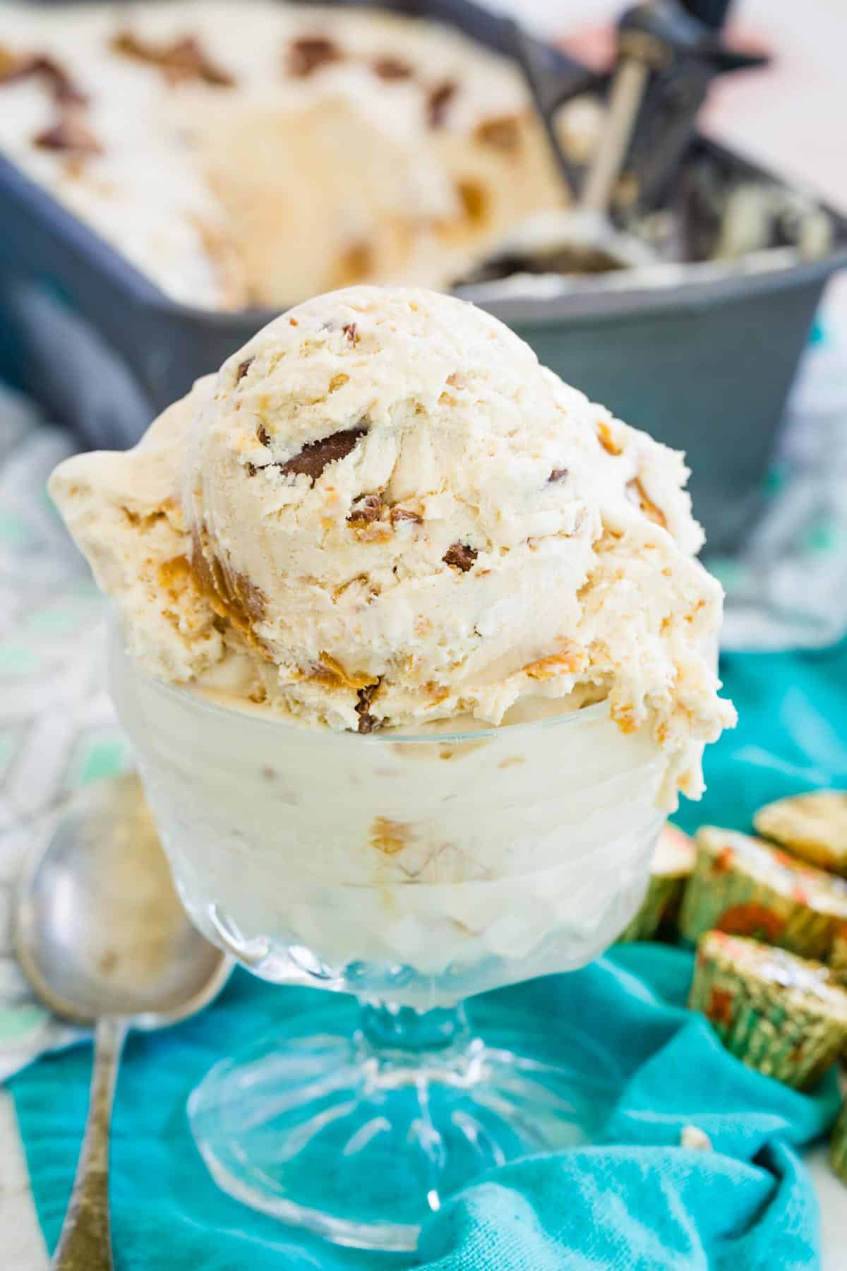 A serving of no-churn Reese's ice cream in a glass ice cream dish, with more ice cream in a loaf pan in the background.