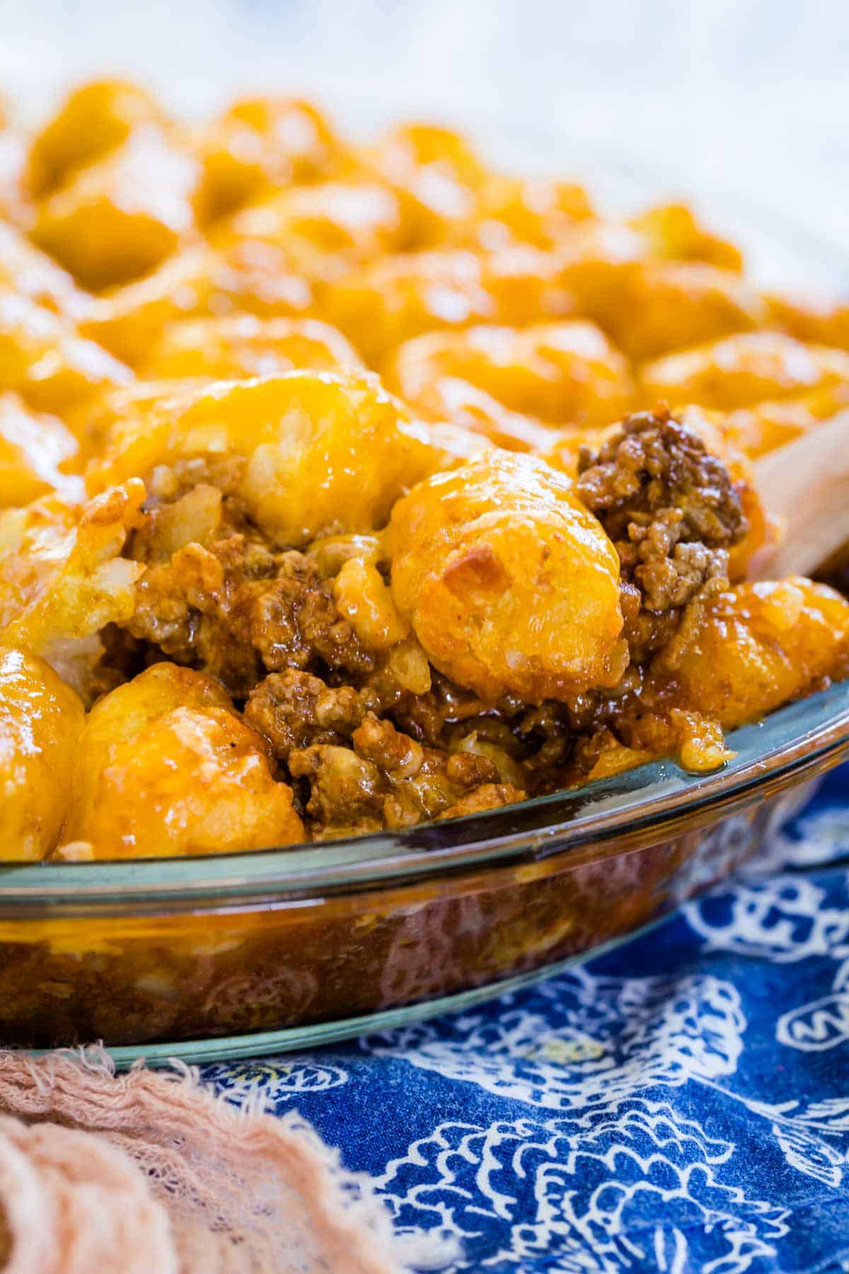 A wooden spoon scoops a serving of sloppy joe tater tot casserole from a baking dish.