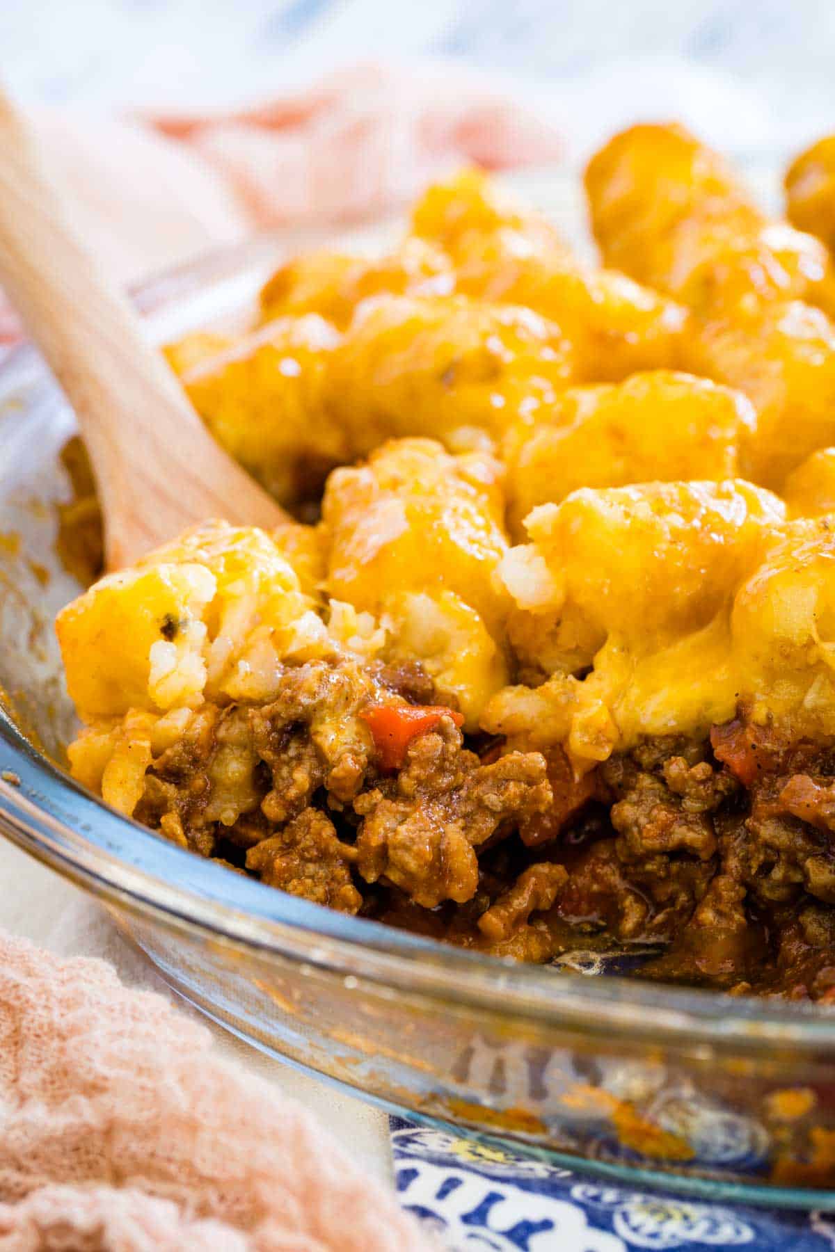 A wooden spoon scoops a serving of sloppy joe tater tot casserole from a baking dish.