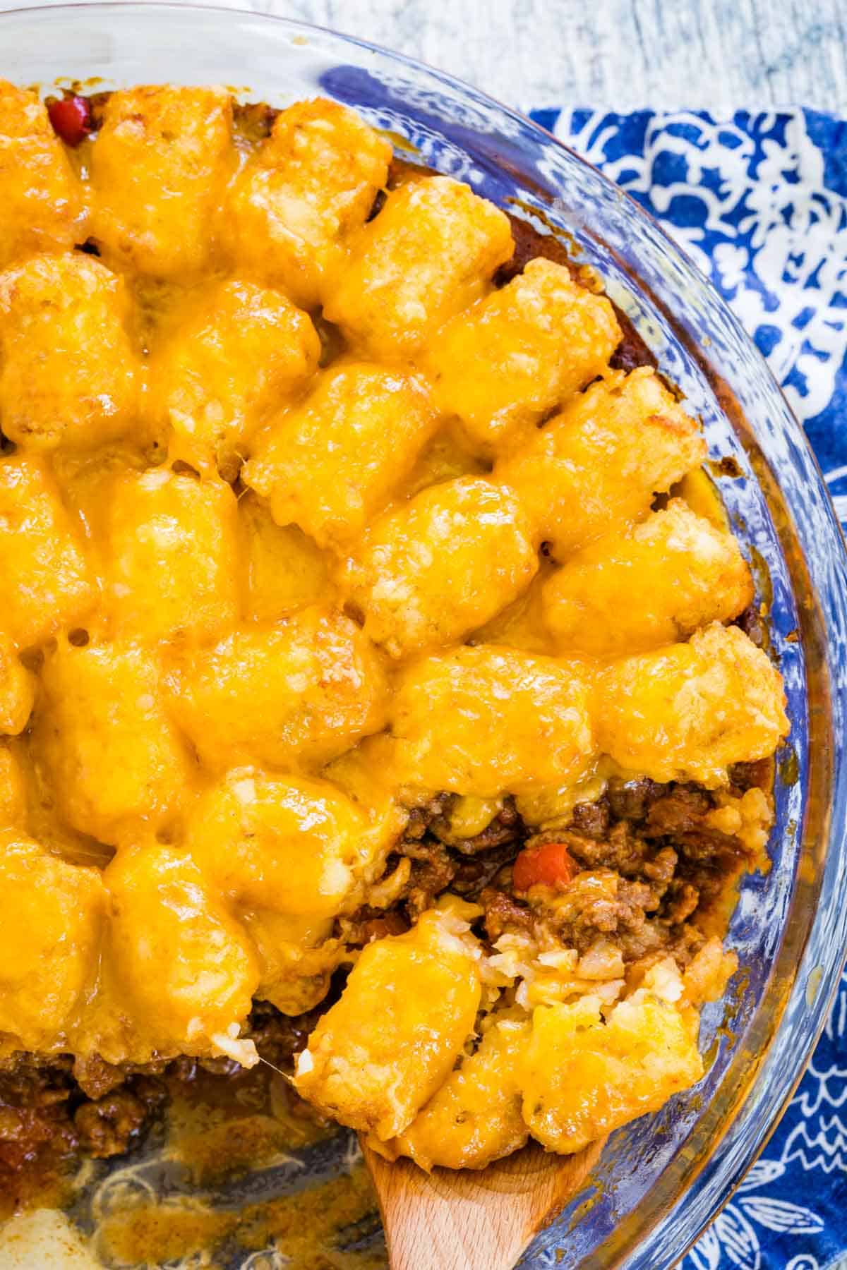 Top view of a wooden spoon scooping a serving of sloppy joe tater tot casserole from a baking dish.