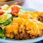 A serving of sloppy joe tater tot casserole on a plate next to a green salad.