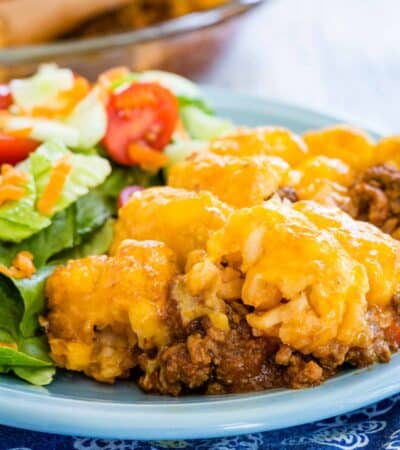 A serving of sloppy joe tater tot casserole on a plate next to a green salad.