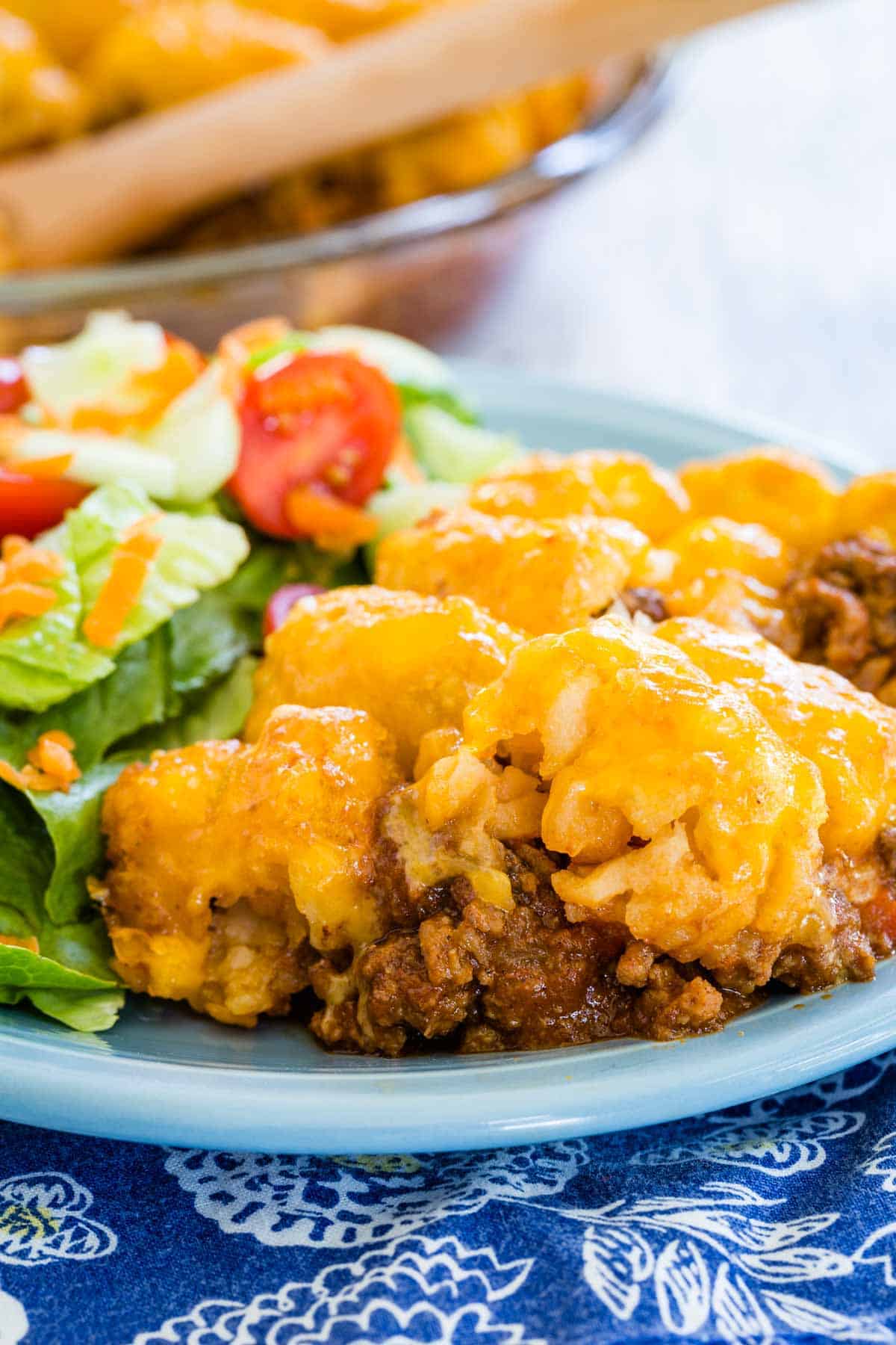 A serving of sloppy joe tater tot casserole on a plate next to a green salad.