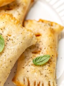 Closeup of pizza rolls piled on a plate and garnished with basil leaves.