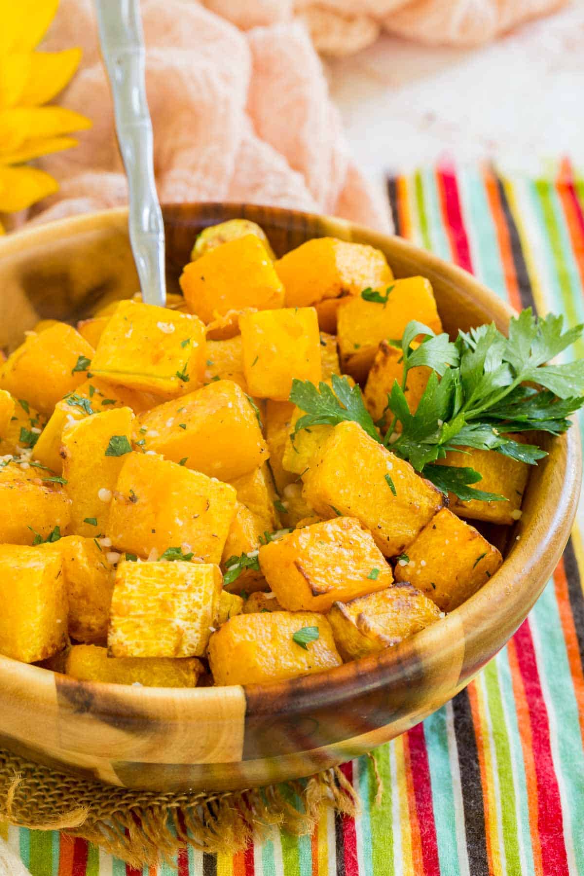 A spoon stuck into a bowl of cubed air fryer butternut squash garnished with fresh green herbs.