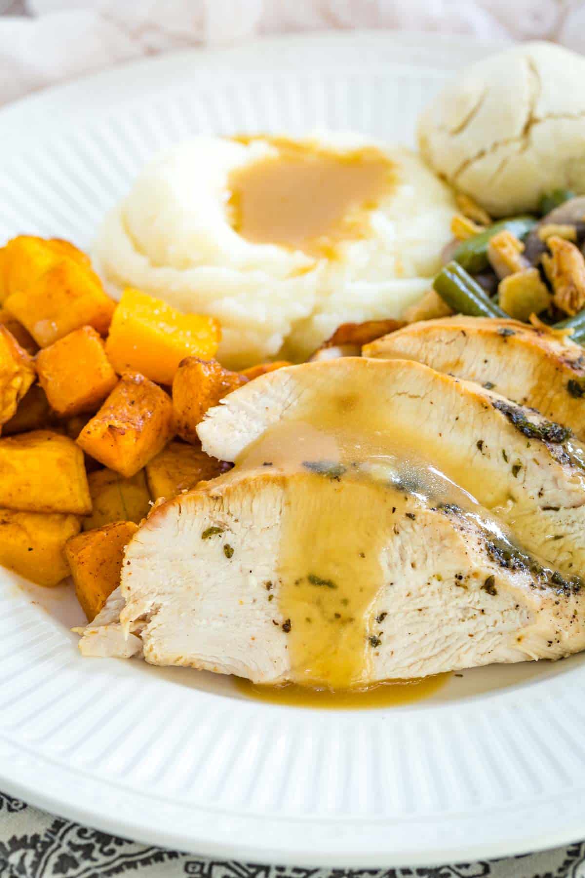 Slices of air fryer turkey with gravy on a white plate next to mashed potatoes, roasted butternut, and green bean casserole.