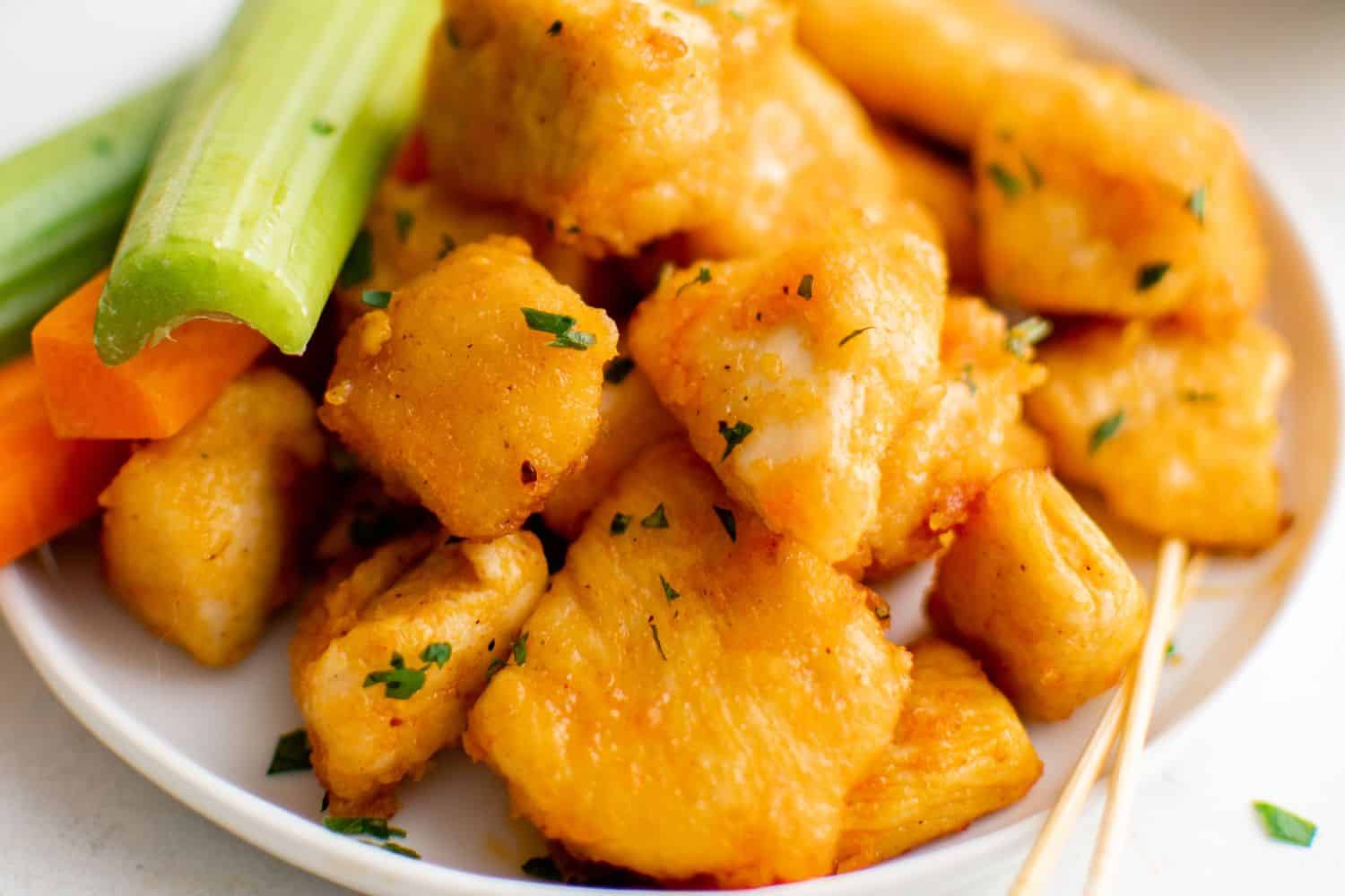 Buffalo chicken bites on a small white plate with a couple of toothpicks and carrot and celery sticks.