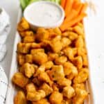 Buffalo chicken bites on a rectangular serving platter with a bowl or ranch dressing and carrot and celery sticks.