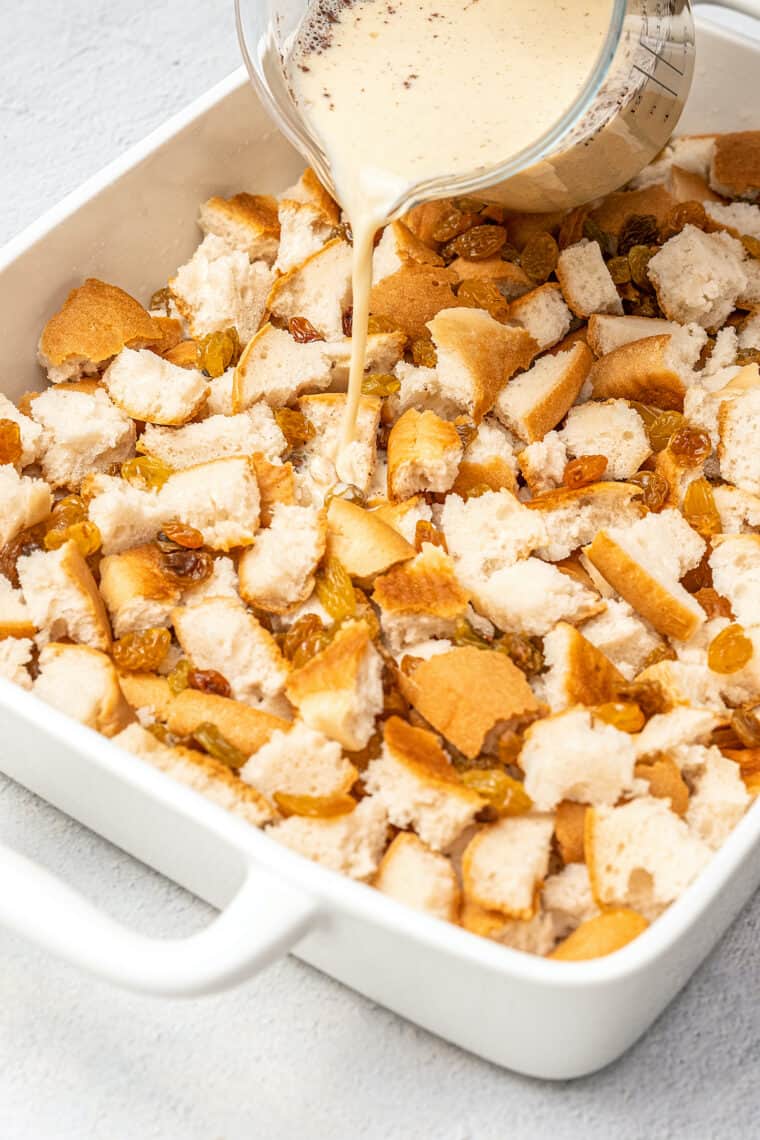 The custard mixture is poured over top of cubed bread and raisins in a baking dish.