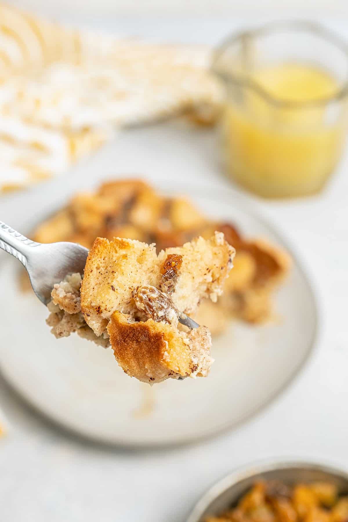 Close up of a forkful of bread pudding with bourbon sauce in the background.