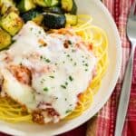 Chicken parmesan served over gluten free pasta on a plate with zucchini.