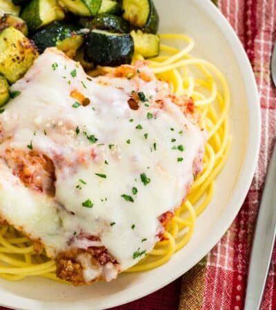 Chicken parmesan served over gluten free pasta on a plate with zucchini.