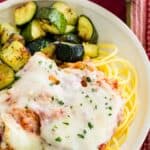 Chicken parmesan served over gluten free pasta on a plate with zucchini with text overlay of the recipe title.
