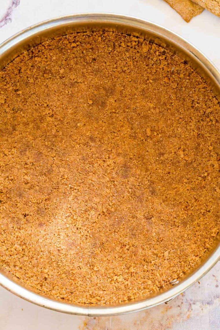 Overhead view of gluten-free graham cracker crust pressed into a springform pan.