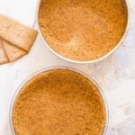 Overhead view of a springform pan and pie plate filled with gluten-free graham cracker crust.
