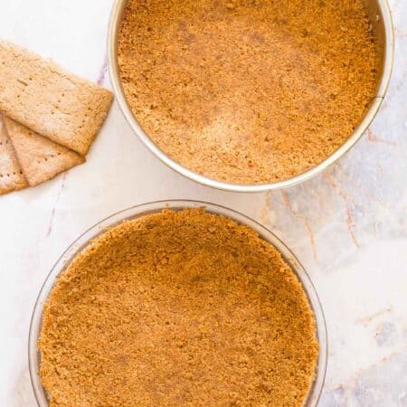 Overhead view of a springform pan and pie plate filled with gluten-free graham cracker crust.