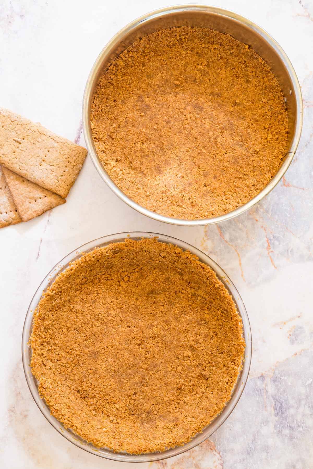 Overhead view of a springform pan and pie plate filled with gluten-free graham cracker crust.