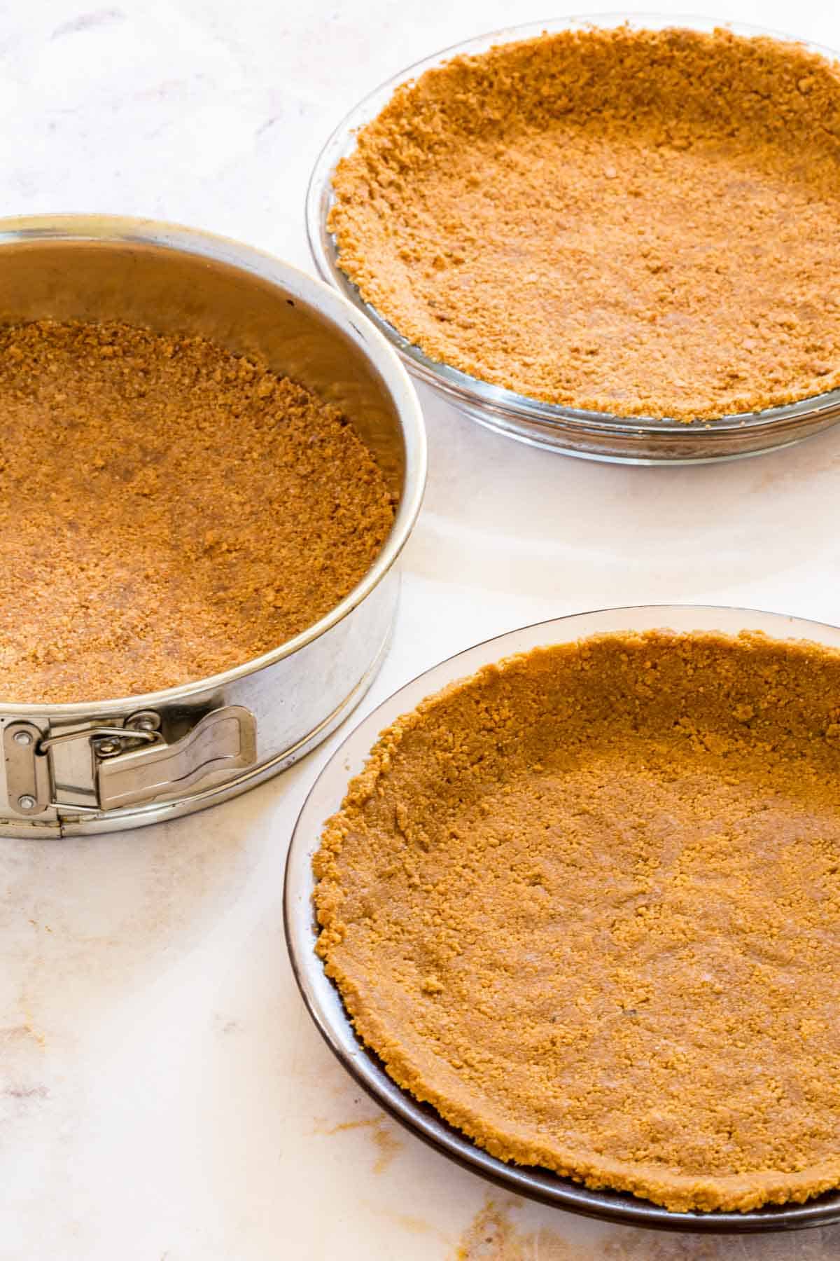 Gluten-free graham cracker crust pressed into two pie plates and a springform pan.