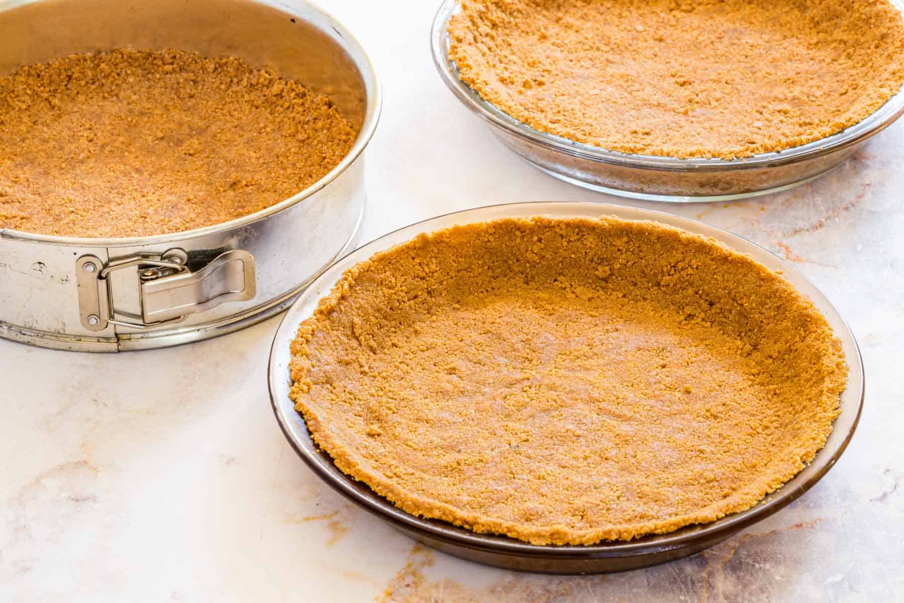 Gluten-free graham cracker crust pressed into two pie plates and a springform pan.